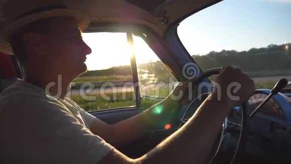 戴帽子的年轻人双手握着方向盘驾驶着一辆带有太阳耀斑的复古汽车高加索人视频的预览图
