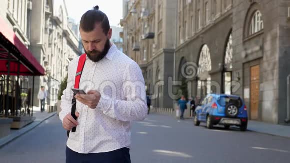 欧洲街头的一个留胡子的男人在他的智能手机上读信息环顾四周视频的预览图