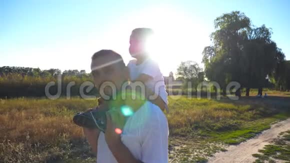 幸福的一家人走在草地上爸爸挥舞着手对着镜头一个金发坐在肩膀上的小男孩视频的预览图