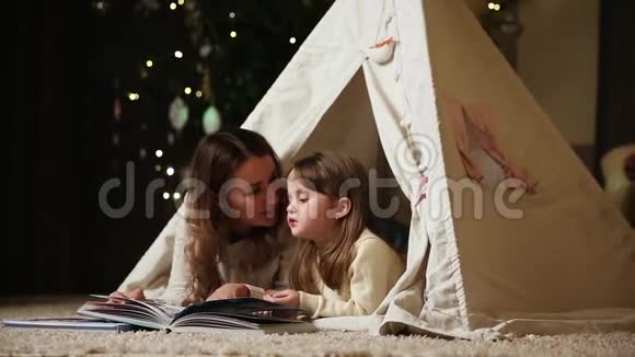 妈妈正在读一个女儿故事因为她和她躺在房子的帐篷里女孩们在微笑视频的预览图