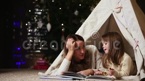 妈妈正在读一个女儿故事因为她和她躺在房子的帐篷里女孩吃果酱视频的预览图