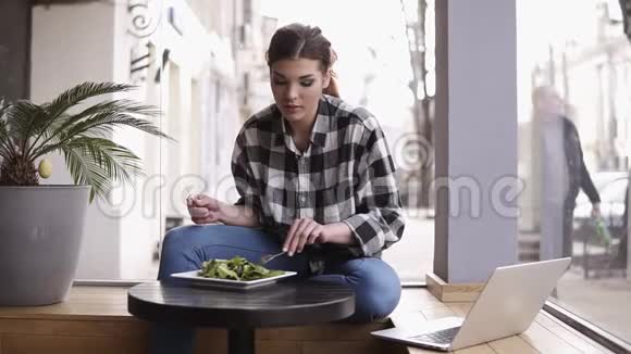 迷人的年轻女人在轻咖啡馆吃午餐享受她的沙拉看着笔记本电脑正面观点视频的预览图