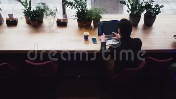 在咖啡馆里用笔记本电脑和智能手机工作的混血男子的俯视图视频的预览图