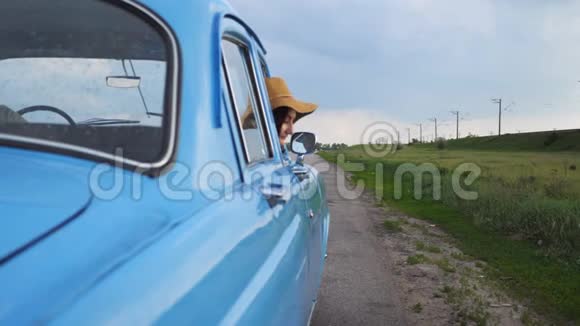 戴帽子的快乐女孩斜倚在复古车窗外微笑着年轻快乐的女人望着老式老汽车的窗外视频的预览图