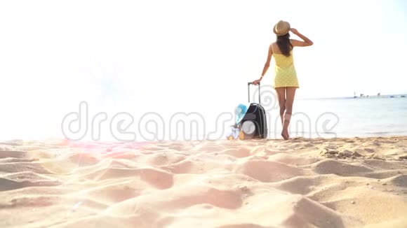 戴着帽子的漂亮女人拿着手提箱站在海滩上看着远处4k视频视频的预览图