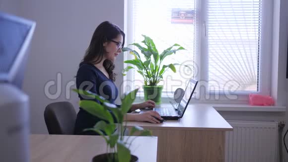 在室内靠近窗户和室内鲜花的办公桌上工作的成功女性视频的预览图