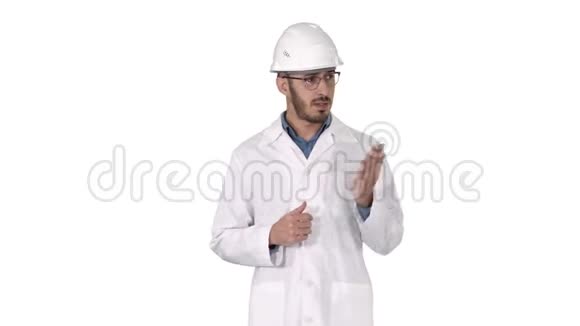 穿着白色长袍和头盔的科学家用手指向侧面并在白色背景上向相机解释视频的预览图
