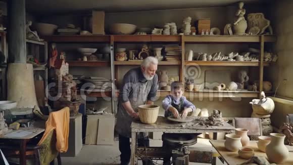 有经验的陶工爱心老人正在小家庭作坊里教他的孙子陶器男孩和他一起工作视频的预览图