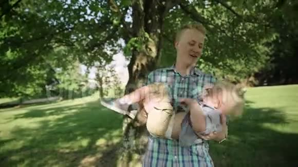 可爱的小男孩女孩和他英俊的年轻爸爸在公园里玩爸爸抱着他的小男孩慢动作全高清视频的预览图