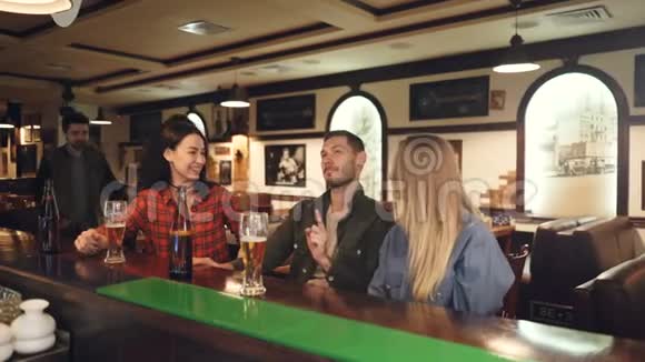 年轻人在酒吧柜台边喝啤酒边聊天这时他们的几个朋友来接他们男人和女人视频的预览图