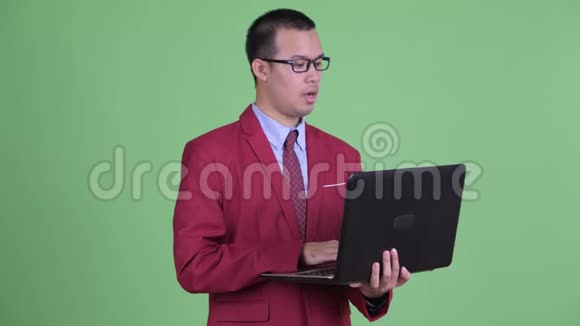 快乐的亚洲商人一边说一边用笔记本电脑视频的预览图
