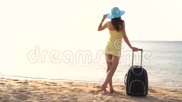 戴着帽子的漂亮女人拿着手提箱站在海滩上看着远处4k视频视频的预览图