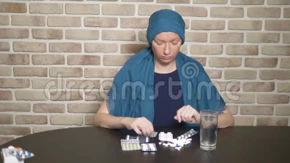 一个戴头巾的女人一个癌症病人接触药丸坐在靠砖墙的桌子旁复制空间视频的预览图