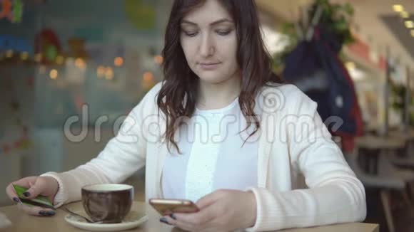 一个漂亮的女人在咖啡馆的桌子上拿着电话和银行卡视频的预览图