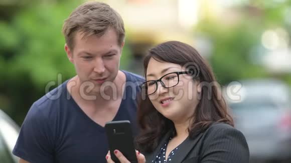成熟的亚洲女商人和年轻的斯堪的纳维亚人一起在户外的街道上使用电话视频的预览图