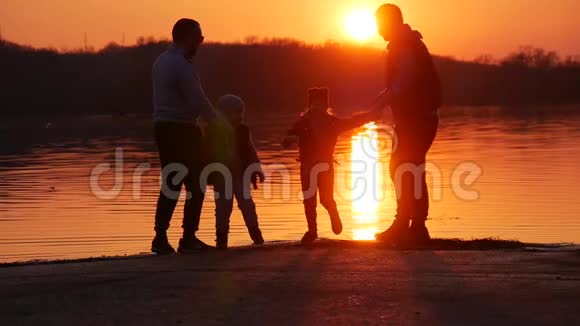 日落时人们在湖上玩耍小朋友和家长的剪影下一次在一起跑步和玩耍视频的预览图