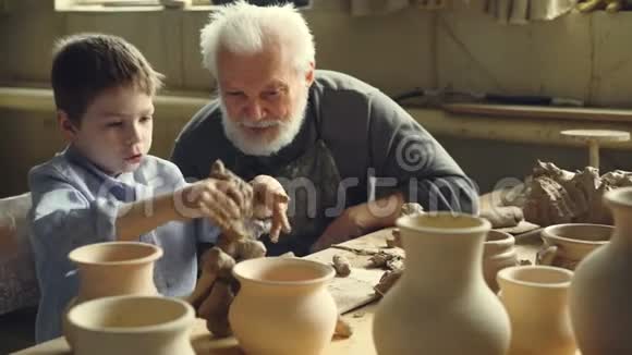 一个严肃的孩子正在捏黏土一边和他的祖父说着专业的陶匠一边坐在桌子旁视频的预览图