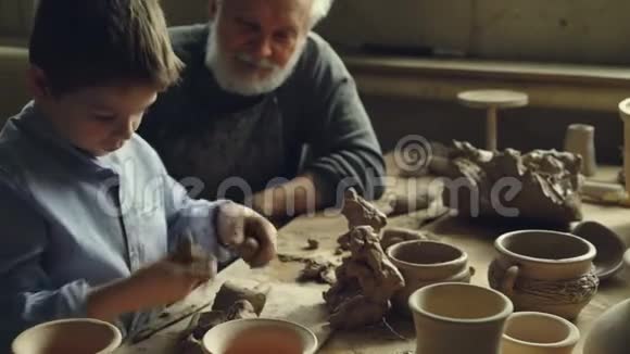 快乐的小孩正在用一大块粘土做玩具躺在桌子上和有经验的爷爷说话视频的预览图
