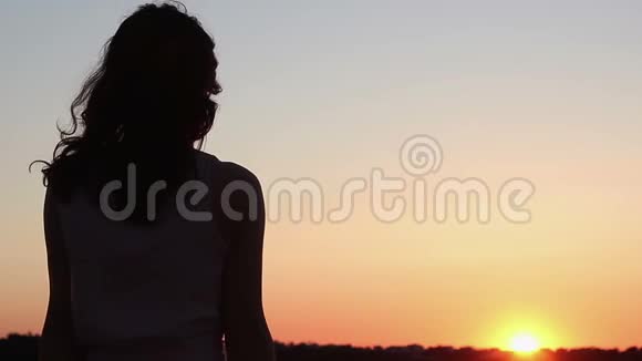 年轻女子望着地平线上令人惊叹的橙色日落想着未来视频的预览图