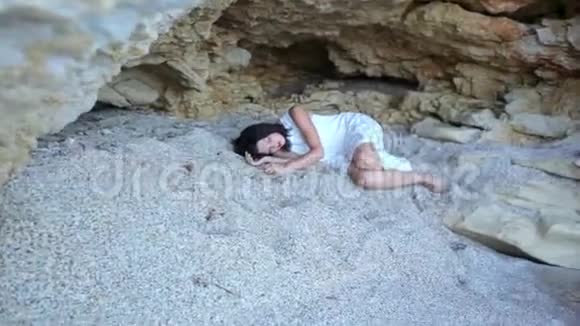 惊魂未定的女孩躺在石窟里的沙滩上海潮向她袭来视频的预览图