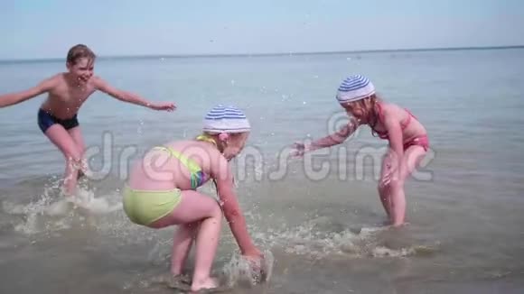 两个女孩和一个男人在海滩上泼水在炎热的夏日里双胞胎泼水欢笑和良好的心情视频的预览图