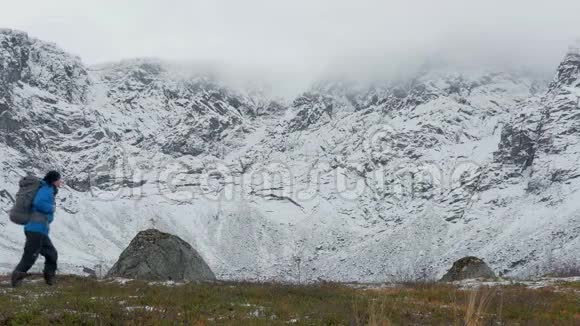 一个背着背包的人独自一人在山里旅行他沿着高高的雪峰走视频的预览图