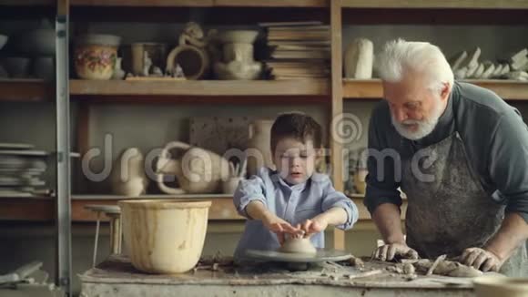 退休爷爷在舒适的家庭作坊里一起工作时给他可爱的小孙子提供陶器的基本知识视频的预览图