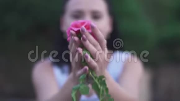 成年女士在花园里闻着粉红色的花视频的预览图