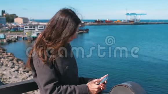 在阳光明媚的秋日布吕内特女士在海边的海边用手机输入一条信息视频的预览图