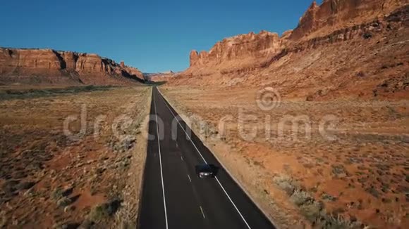 无人机照相机跟随银车沿着笔直的沙漠公路在美国令人惊叹的岩石山景观中行驶视频的预览图