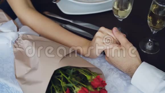 用香槟杯和鲜花紧紧握住和挤压桌子上的雄性手的特写镜头浪漫浪漫视频的预览图