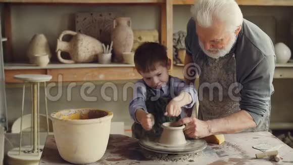 好奇的男孩正在小家庭工作室里向他有经验的祖父学习陶器小孩正在制作陶罐视频的预览图