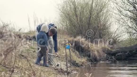 父子俩一起在河上钓鱼岸上拿着鱼竿的小男孩视频的预览图