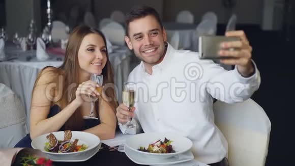 有魅力的情侣在餐厅吃饭时用智能手机用香槟杯自拍视频的预览图