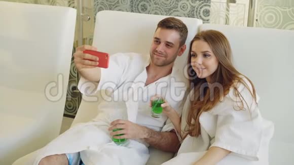 迷人的情侣正在使用智能手机用鸡尾酒杯自拍同时在水疗沙龙放松他们是视频的预览图