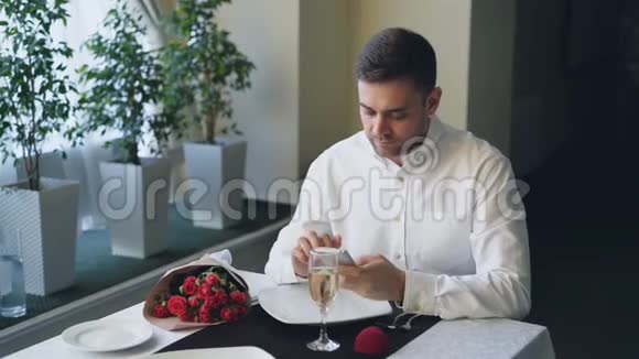 穿着得体的愤怒的年轻人正在餐馆等他的女朋友用智能手机打开珠宝盒视频的预览图