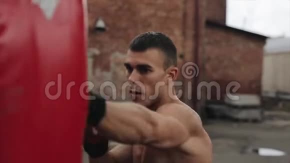 肌肉男拳击手练习拳打脚踢的近距离侧视拳击袋在户外视频的预览图
