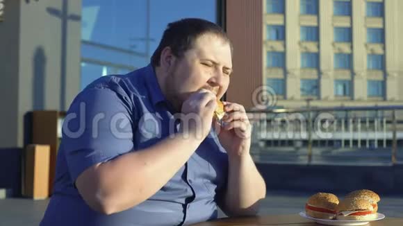 胖子咬快餐汉堡在户外咖啡馆吃晚餐暴饮暴食视频的预览图