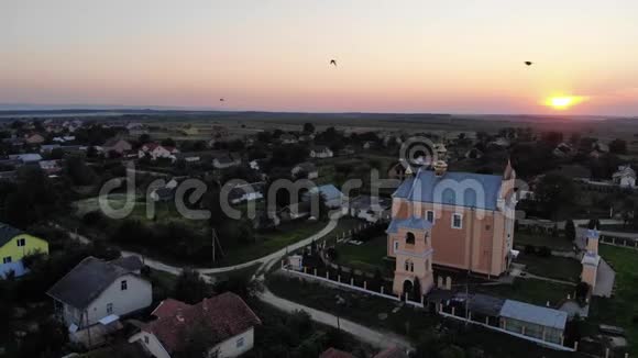 古老的基督教寺和钟楼附近燕子在天空中飞翔日落乌克兰村庄的空中景色视频的预览图