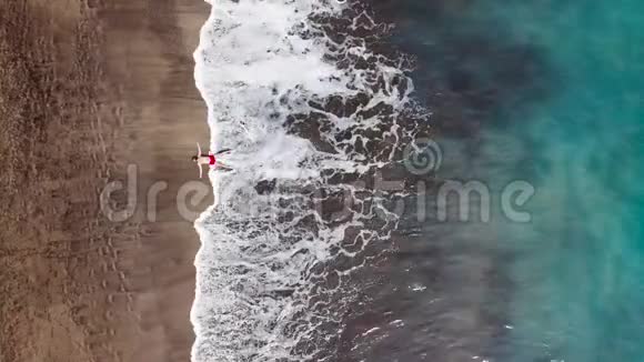 一个穿着红色短裤的男人的鸟瞰图躺在废弃的黑色火山海滩上摆出一个明星的姿势空中无人驾驶飞机的海上镜头视频的预览图