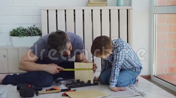有胡子的人在和儿子一起做建筑工程然后又在做击掌工程的时候正在用尺尺板测量木头视频的预览图