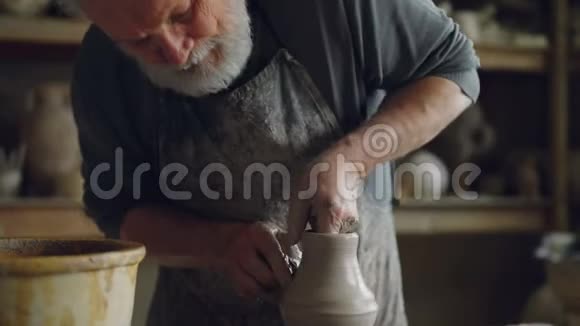 辛勤工作的资深陶工正在用水把手放在碗里润湿并在旋转的投掷轮上触摸粘土罐有胡子视频的预览图