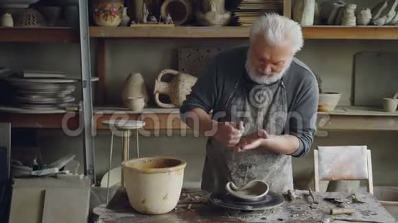 创意雕塑家站在他的车间里的工作桌前正在制作不寻常的大碗有胡子的老人视频的预览图