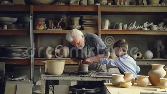 专业的男陶匠正在和粘土一起工作用他好奇的孙子帮助他旋转投掷轮陶瓷视频的预览图