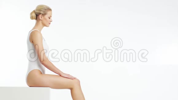 年轻美丽健康和自然的金发女人穿白色泳衣涂上保湿霜按摩护肤视频的预览图