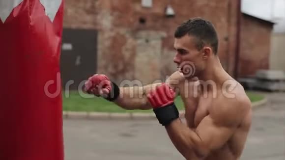 肌肉男拳击手练习拳打脚踢的近距离侧视拳击袋在户外视频的预览图