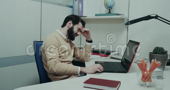 办公室里辛苦的一天年轻人坐在他的桌子上紧张地看着笔记本电脑视频的预览图