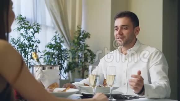 年轻的帅哥正和女友在餐馆约会喝着香槟带着她的爱牵手视频的预览图