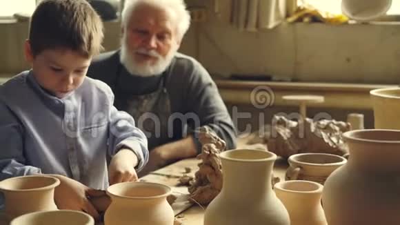 小男孩正和爷爷奶奶坐在家里的陶器工作室里的桌子上玩粘土爷爷在跟我说话视频的预览图
