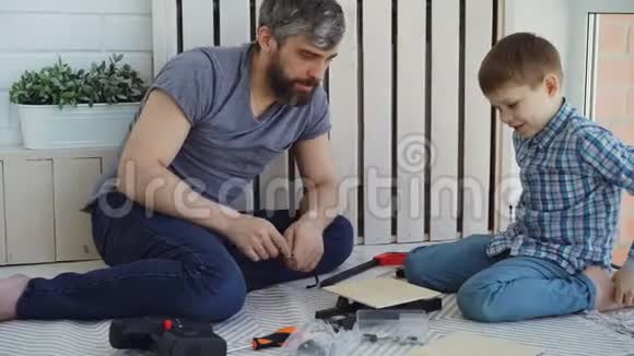 友好的父亲和小儿子在家里坐在地板上做建筑工程时谈笑风生视频的预览图